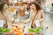 Waist up portrait of young woman choosing fresh organic fruits while buying groceries at farmers market or supermarket, copy space on right