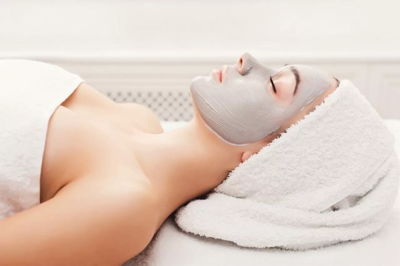 Face mask, spa beauty treatment. Woman applying facial clay mask at spa salon, skincare, top view, overhead