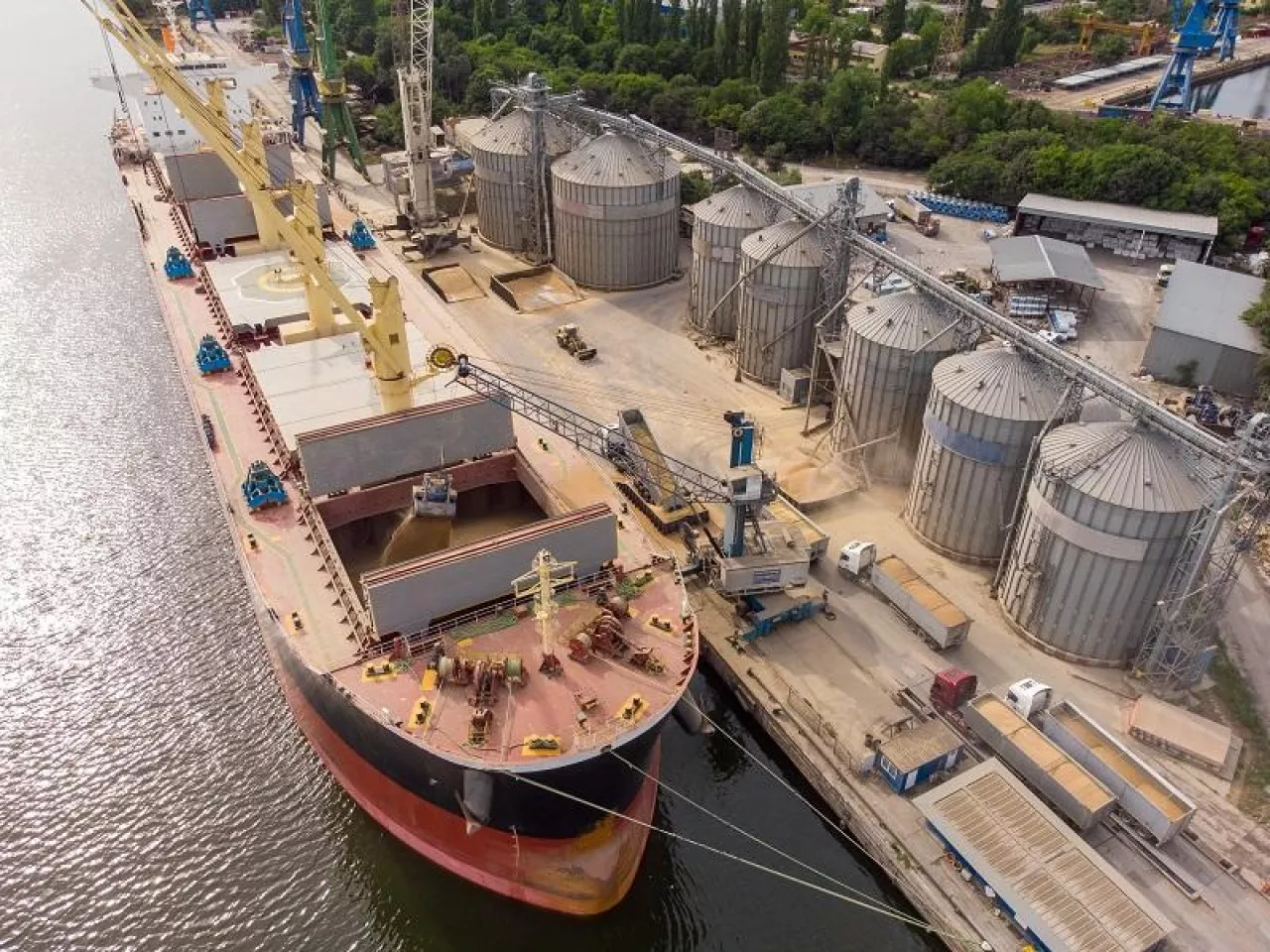 Loading grain into holds of sea cargo vessel in seaport from silos of grain storage. Bunkering of dry cargo ship with grain. Aerial top view