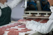 Female butcher processing hamburger patty at meat factory