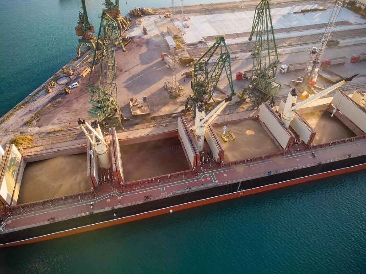 Aerial top view of big cargo ship bulk carrier is loaded with grain of wheat in port at sunset