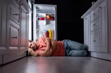 exhausted young man sleeping on kitchen floor near open refrigerator