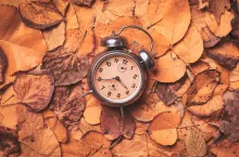 Vintage alarm clock on pile of dry autumn leaves for daylight saving time change in fall, flat lay top view