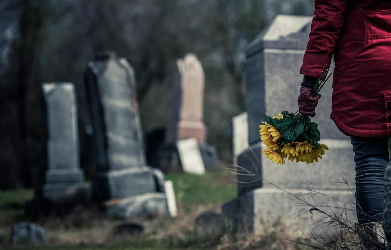 Close-up of a Sad Woman Holding Sunflowers in front of a Loved one‘s Gravestone. Focus on the Bouquet.