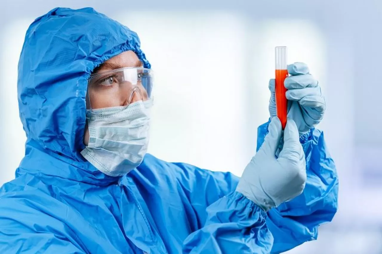 Medic in hazmat protective suit holds a test tube with a coronavirus positive blood sample from Wuhan, China. 2019 nCoV pandemic. stop coronavirus. MERS. A virologist is thinking of a coronavirus vaccine. influenza, bird flu