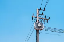 AC high-voltage power transformer on electric pole with wires on a background of blue sky, high voltage transmission line.