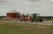 Nowoczesna biogazownia rolnicza w otoczeniu gospodarstwa. Na pierwszym planie ciągnik Fendt z przetrząsaczem/zgrabiarką, a w tle czerwona instalacja biogazowa z kopulastym dachem. Obraz ukazuje potencjał odnawialnych źródeł energii na wsi oraz rolniczą infrastrukturę technologiczną.