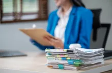 Company employee holding accounting bookkeeping documents checking financial data or marketing report working in office with laptop. Paperwork management