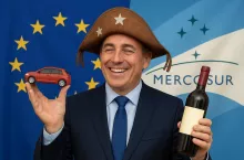 Fotorealistyczna grafika przedstawiająca uśmiechniętego mężczyznę w kapeluszu cangaceiro – tradycyjnym nakryciu głowy z brazylijskiego regionu Nordeste – trzymającego w dłoniach czerwony samochodzik i butelkę wina. W tle przenikające się flagi Unii Europejskiej i Mercosur, symbolizujące zbliżającą się umowę handlową. Postać reprezentuje zwycięzców porozumienia – przemysł motoryzacyjny i winiarski – kontrastujących z pomijanym głosem rolników.