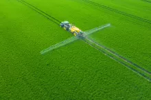 Widok z lotu ptaka na ciągnik z opryskiwaczem polowym podczas oprysku zielonego pola zbóż.