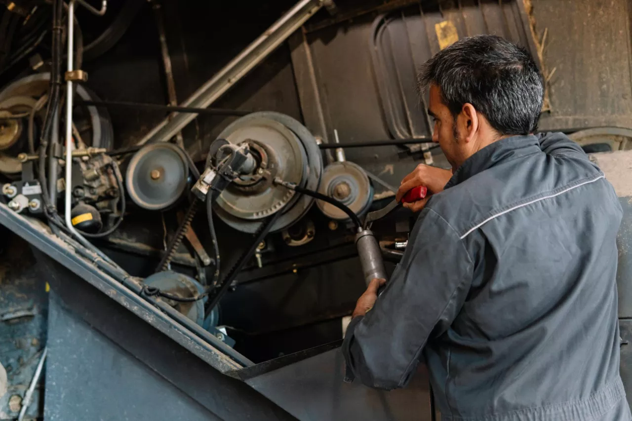 Mechanic greasing combine harvester gears using grease gun during maintenance in a farm