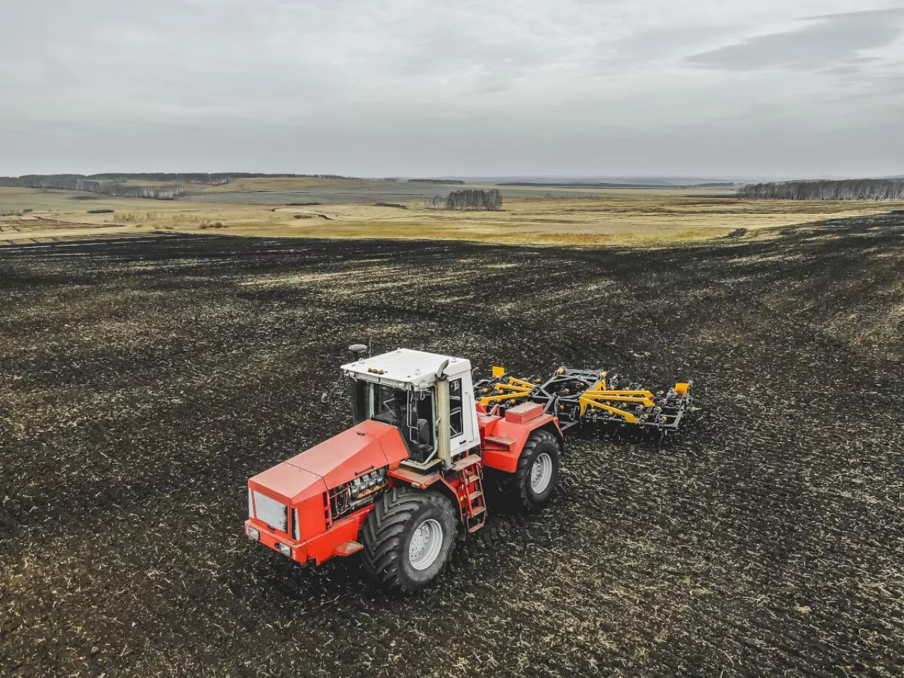 Traktor pracujący na szerokim polu czarnoziemu. Krajobraz typowy dla dużych areałów Ukrainy, gdzie dominują uprawy w monokulturach i intensywna produkcja roślinna.