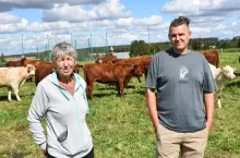 Piotr Czepek (po prawej) oraz jego matka Krystyna Czepek stoją na pastwisku z wielorasowym stadem bydła w tle.