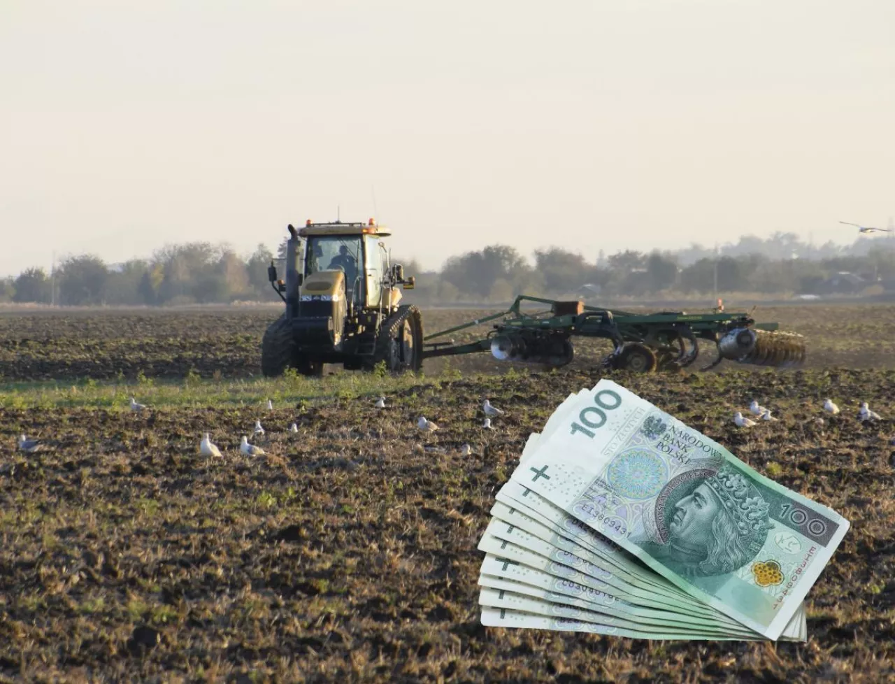 Stos banknotów 100 złotych na tle pola uprawnego po orce. W tle ciągnik z broną talerzową podczas jesiennej uprawy gleby.