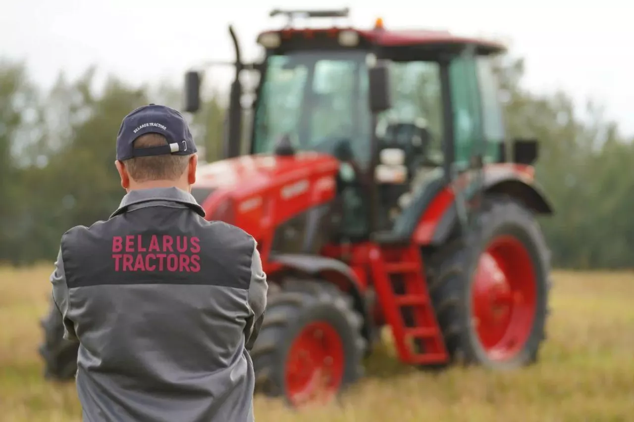 Mężczyzna w polarze z napisem ”Belarus Tractors”, w tle czerwony ciągnik MTZ Belarus.