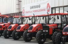 Różne modele ciągników marki Ursus stoją w rzędzie na placu przed budynkiem