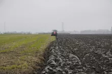 Ciągnik orzący pole – widoczna granica między zaoraną ziemią a nieuprawioną częścią pola.