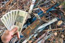 Złom metalowy na skupie – na tle prętów i elementów stalowych dłoń trzyma banknoty 100 zł, symbolizujące ceny złomu.