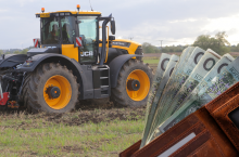 Ciągnik rolniczy pracujący w polu, na pierwszym planie portfel z banknotami – symbol kosztów lub finansowania w rolnictwie.