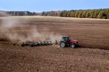 Ciągnik rolniczy wykonujący orkę pola uprawnego z wykorzystaniem pługa wieloskibowego. Widok z góry na prace polowe na dużej powierzchni gruntu.