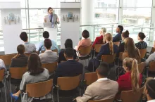 High angle view of Caucasian male speaker with laptop in front of diverse group of business people sitting at business seminar in office building