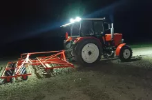 Ciągnik MTZ-82 z zaczepionym agregatem uprawowym podczas pracy na polu w nocy