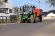 Ciągnik John Deere 5105M jedzie z przyczepą rolniczą