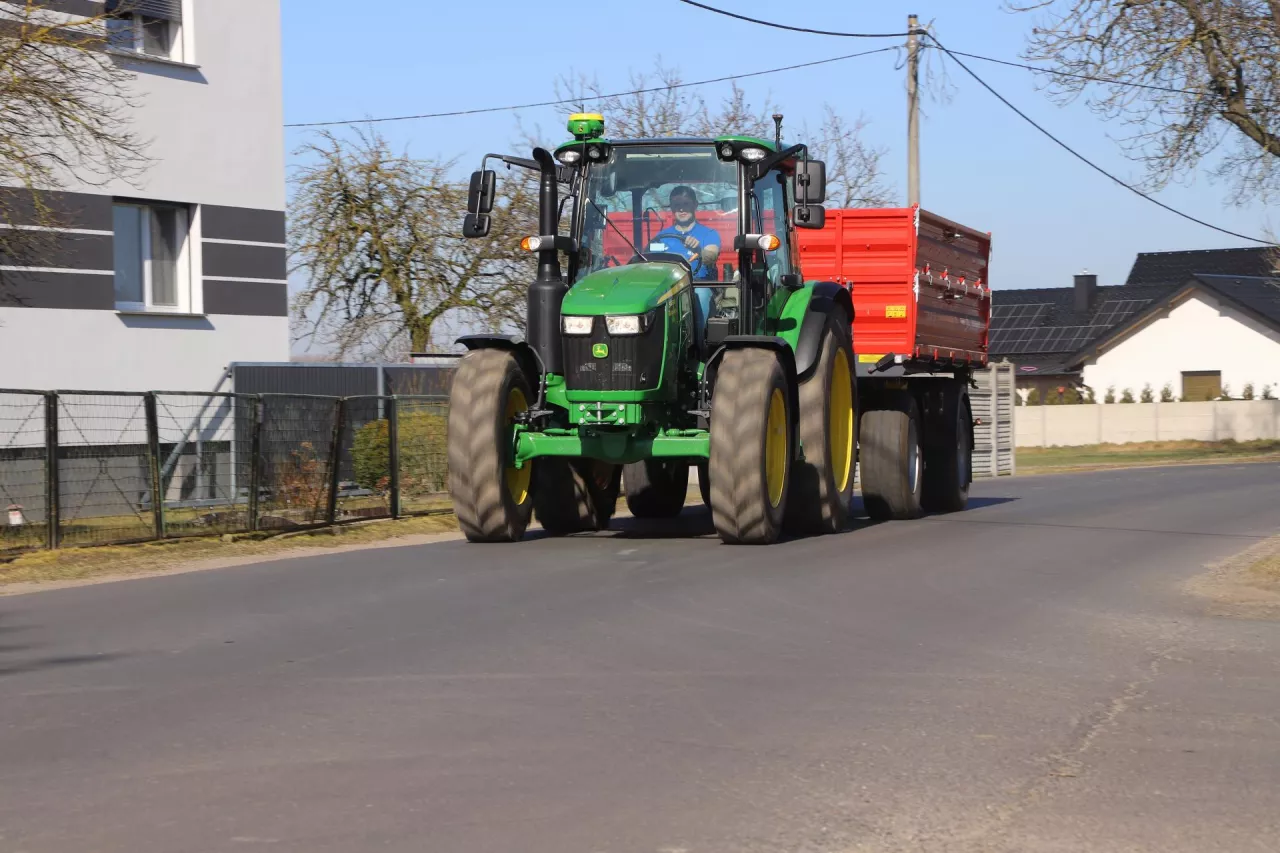 Ciągnik John Deere 5105M jedzie z przyczepą rolniczą