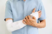 Young man with gauze bandage wrapped around injury hand on white background